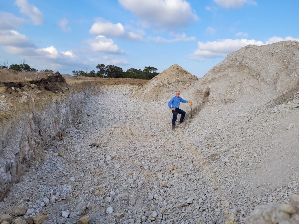 A man stands in a large pit of gravel in an agricultural landscape.